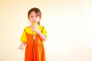 Lovely baby girl wears yellow-orange outfit gokowa outfit or Mugunghwa, and hold gold microphone singing music. Girls and teen fashion dress. photo