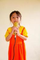 Lovely baby girl wears yellow-orange outfit gokowa outfit or Mugunghwa, and hold gold microphone singing music. Girls and teen fashion dress. photo