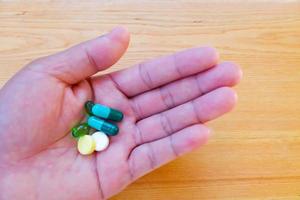 pastillas de colores y medicamentos en la mano sobre la mesa de madera. foto