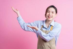 Young Asian waitress standing on pink background photo