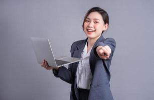 Young Asian business woman wearing suit and using laptop on gray baclground photo