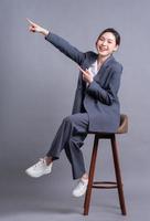 Young Asian businesswoman sitting on chair and posing on gray background photo