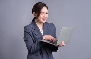 Young Asian business woman wearing suit and using laptop on gray baclground photo