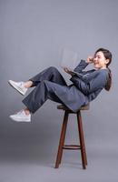 Young Asian businesswoman sitting on chair and using laptop on gray background photo