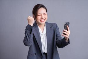 Young Asian businesswoman holding smartphone on gray background photo