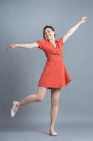 Full length image of young Asian woman wearing orange dress on gray background photo