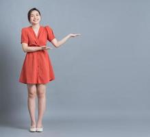 Full length image of young Asian woman wearing orange dress on gray background