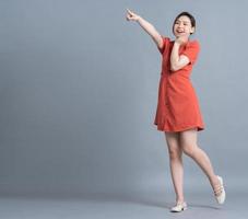 Full length image of young Asian woman wearing orange dress on gray background photo