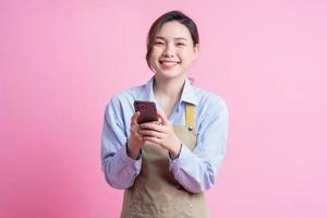 Young Asian waitress standing on pink background photo