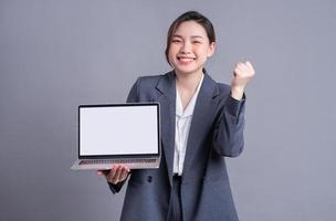 Young Asian business woman wearing suit and using laptop on gray baclground photo