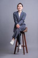 Young Asian businesswoman sitting on chair and posing on gray background photo