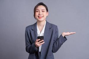 Young Asian businesswoman holding smartphone on gray background photo