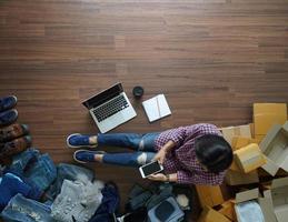 vista superior de las mujeres que trabajan con teléfonos inteligentes desde casa en un piso de madera con paquete postal, vendiendo el concepto de ideas en línea foto