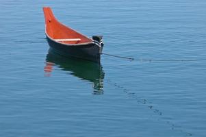 Orange rowing boat floats on calm lake photo