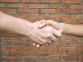 Close-up of shaking hands between man and woman with brick background photo