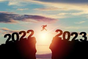 Welcome merry Christmas and happy new year in 2023,Silhouette Man jumping from 2022 cliff to 2023 cliff with cloud sky and sunlight. photo