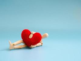 Wooden puppet hugging red heart and fall down on the floor. copy space for text and content. concept of love and Heart attack and Health Problems photo