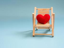 corazón rojo de hilo en la silla de playa de madera sobre fondo de pantalla azul aislado. copie el espacio para el texto. día de san valentín, concepto de amor y fondo de amor foto
