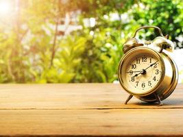 Vintage alarm clock on wood table. The background is green from tree and light bokeh photo