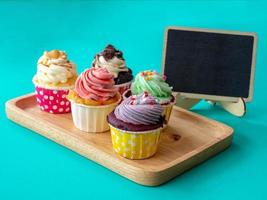 Colorful of homemade cupcake with empty blackboard and copy space for your text. Cupcake on wooden Tray on green background. photo