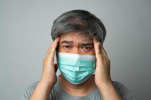 Sick Asian man wearing a medical face mask and Take a hand to hold the headache in the head. Concept of protection pandemic coronavirus and respiratory disease photo