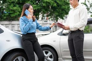 Asian women driver Talk to Insurance Agent for examining damaged car and customer checking on report claim form after an accident. Concept of insurance and car traffic accidents. photo