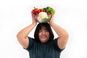 Happy Asian overweight woman holding a vegetable basket and smiling on isolated white background, Concept of good health comes from eating a nutritious diet. photo