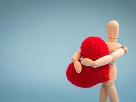 Wooden puppet standing and holding a red heart on the blue screen background. Wooden puppet holding the heart with love and care. Concept of take care and love. photo