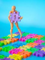 action figure stand on colorfull plastic number and hold purple plastic number one on blue background. Concept of education. copy space for text and content. photo