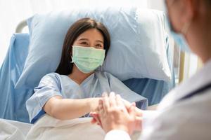 las doctoras asiáticas sostienen la mano del paciente y alientan y brindan asesoramiento médico mientras verifican la salud del paciente en la cama. concepto de cuidado y compasión foto