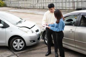 la conductora asiática habla con el agente de seguros para examinar el automóvil dañado y el control del cliente en el formulario de reclamo de informe después de un accidente. concepto de seguros y accidentes de tráfico de automóviles. foto