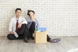 Two male employees sat on the floor talking in front of each other with a cardboard box for personal use after being fired from work. photo