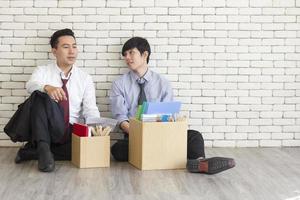 Two male employees sat on the floor talking in front of each other with a cardboard box for personal use after being fired from work. photo