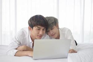 A male couple with an Asian man lying on their laptops happily in bed, expressing openly gay men accepting LGBT concepts. photo