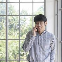 un joven empresario asiático se para en el balcón de una ventana hablando por teléfono. foto