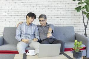 un padre y un hijo asiático sentados en el sofá y charlando en una videollamada en una laptop. foto