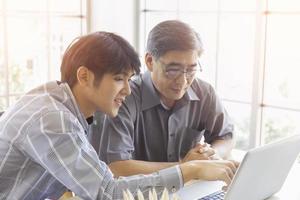 An elderly Asian man is learning how to trade online through the Internet with a young man who teaches him. photo