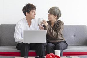 una pareja masculina y un hombre asiático se sientan en el sofá con su amor mutuo y juegan juntos con sus computadoras portátiles. foto