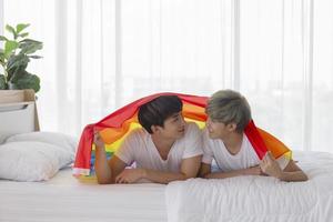 Male and Asian couples lay on their heads a multicolored flag bearing LGBT signs, expressing openly gay men accepting LGBT concepts. photo