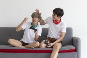 A male couple with an Asian man sitting on a sofa playing video games having fun. photo