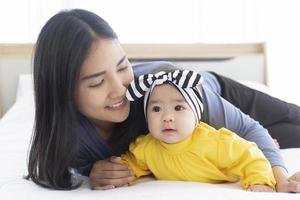 An Asian mom plays with her baby in bed with love and care. photo