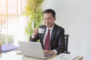 The manager of an Asian man sipping coffee on his desk in a radiant manner. photo