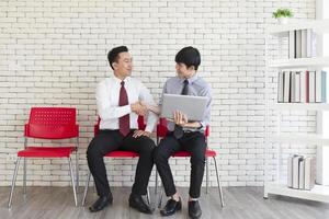 Two Asian men sit on red plastic chairs waiting for a job interview. photo
