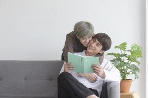 A male couple with an Asian man cuddling on the sofa with their love for one another and the other reading a book. photo