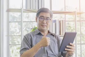 An Asian middle-aged man using an iPad in his hand feels great. photo