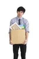 An Asian man stands sad on a white background after being fired, keeping his personal belongings in a carton box. photo