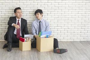 dos empleados varones se sentaron en el suelo hablando uno frente al otro con una caja de cartón para uso personal después de ser despedidos del trabajo. foto