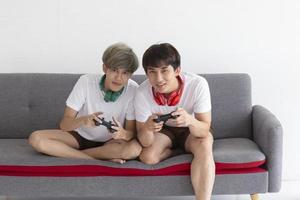 A male couple with an Asian man sitting on a sofa playing video games having fun. photo