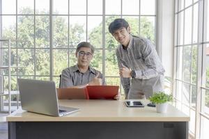 An Asian middle-aged man with his son standing next to a desk in the office. photo