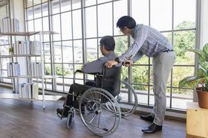 un padre asiático de mediana edad se sienta en una silla de ruedas y tiene un hijo a su lado. foto